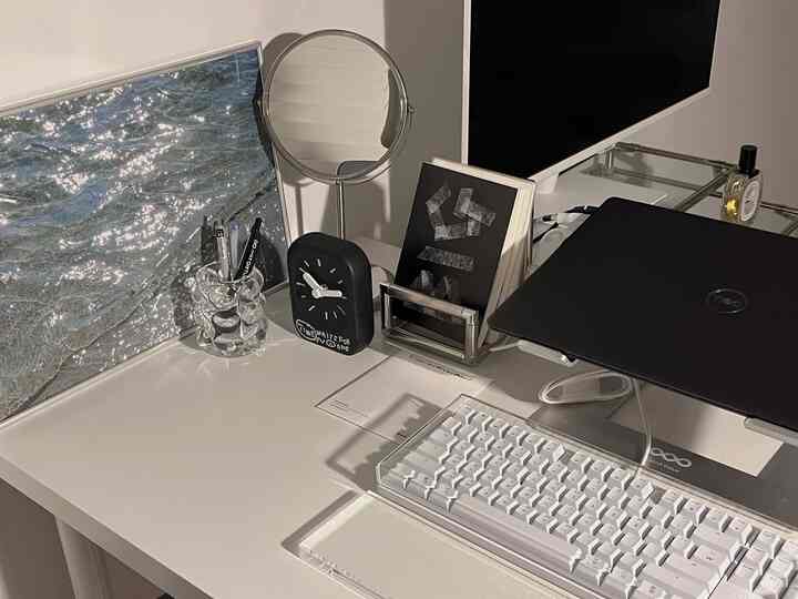 白を基調としたモダンなホームオフィスのデスク、黒い時計と白いキーボードが整然と配置された印象的な空間