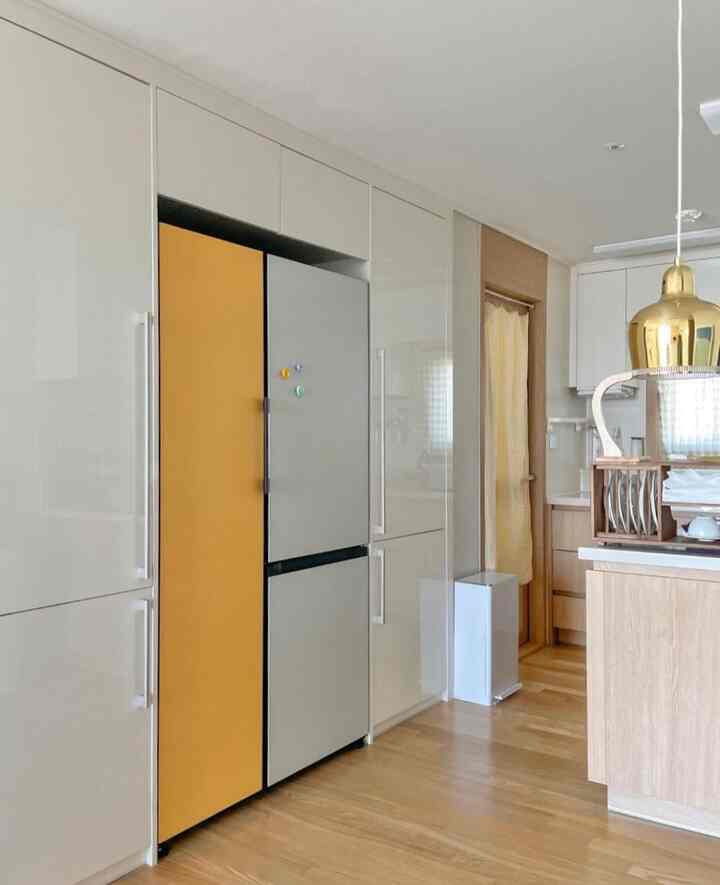 Modern kitchen with natural wood tones and yellow accent, featuring a striking gold Artek pendant light in a clean setting