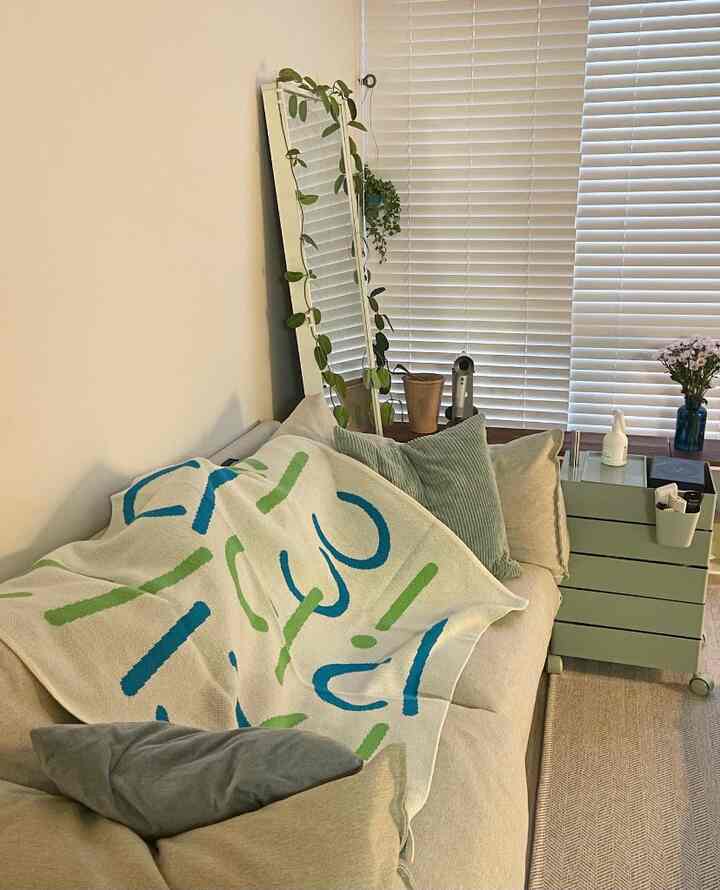 Natural-toned living room featuring beige sofa with colorful throw, full-length mirror, and side table creating cozy atmosphere