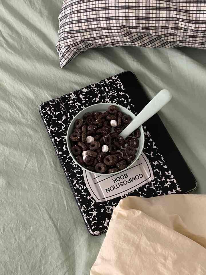 Soft green and beige toned bedroom with plaid pillow, a bowl of chocolate cereal with white spoon resting on bed, creating a cozy vibe