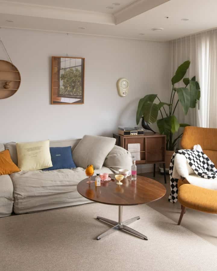 Beige and light brown toned living room featuring sofa, round coffee table, yellow armchair, and plants with warm atmosphere