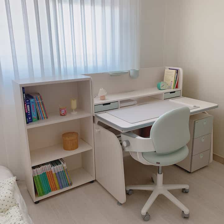 Natural-toned kids' room with white elementary school desk, chair, bookshelf, and storage units creating a neat study area