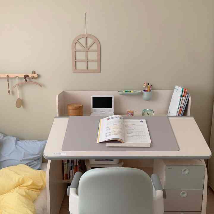 A pastel and natural toned kids' room featuring a centrally positioned adjustable kids' desk with a simple and neat study setup