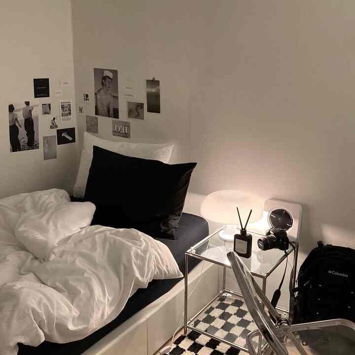 Black and white toned bedroom featuring a neat bed, glass side table, and checkerboard rug in a modern, simple setting