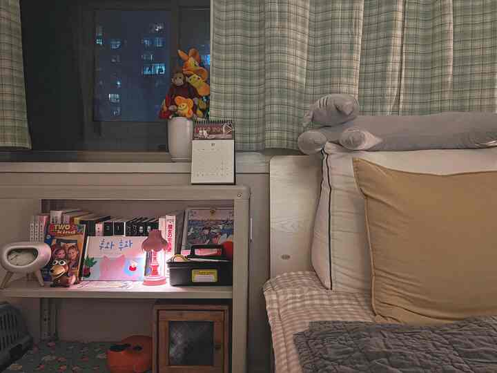 Natural color bedroom featuring bed with pillows and duvet cover, a shelf with books and a curtain-covered window, creating a cozy atmosphere