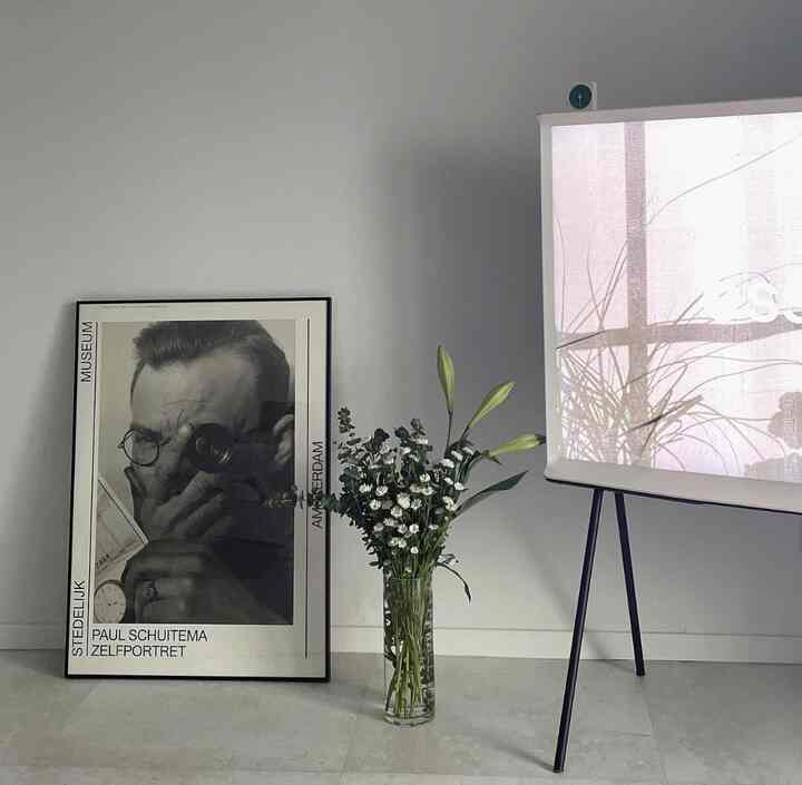 Minimal entrance space in white and black tones featuring a black-and-white poster leaning against the wall and a transparent vase with flowers, creating a clean interior