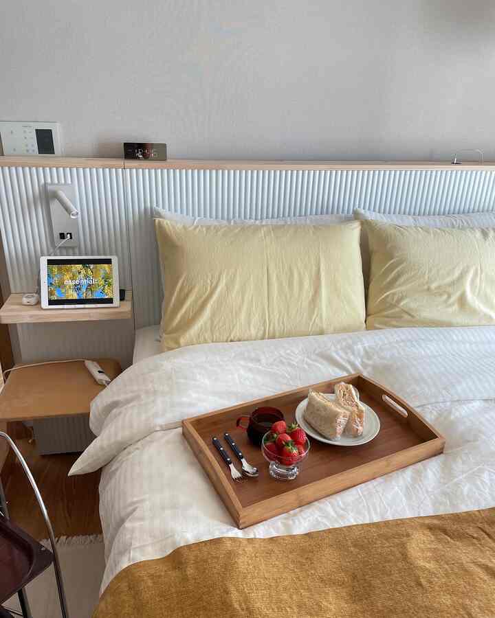 White and wood tone bedroom featuring yellow pillows and a wooden tray on a cozy bed