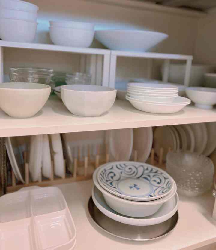 白とナチュラルカラーのキッチン棚にシンプルで素朴な器が整然と並べられた印象的な空間