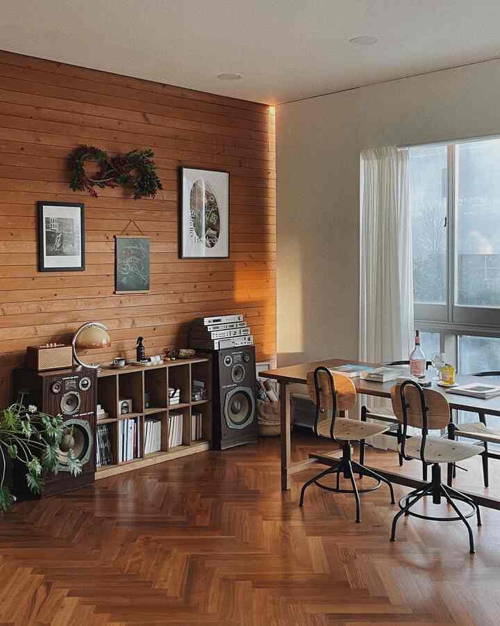 Cozy study featuring warm wood tone walls and flooring, bookshelf with Bluetooth speakers, long wooden table with chairs, creating a natural and inviting atmosphere
