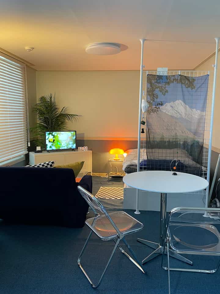 白と青のトーンのワンルーム、ベッドとソファ、透明な椅子が配置されたミニマルで居心地の良いインテリア