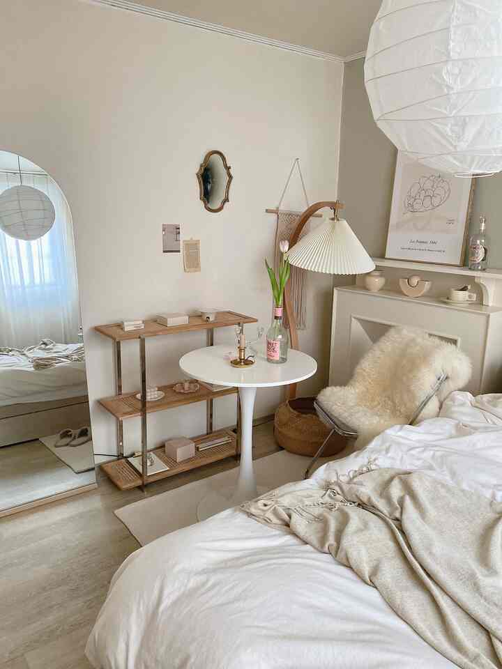 A white and wood tone bedroom featuring a round table, arch-shaped full-length mirror, rattan shelf, and a cozy sheepskin rug