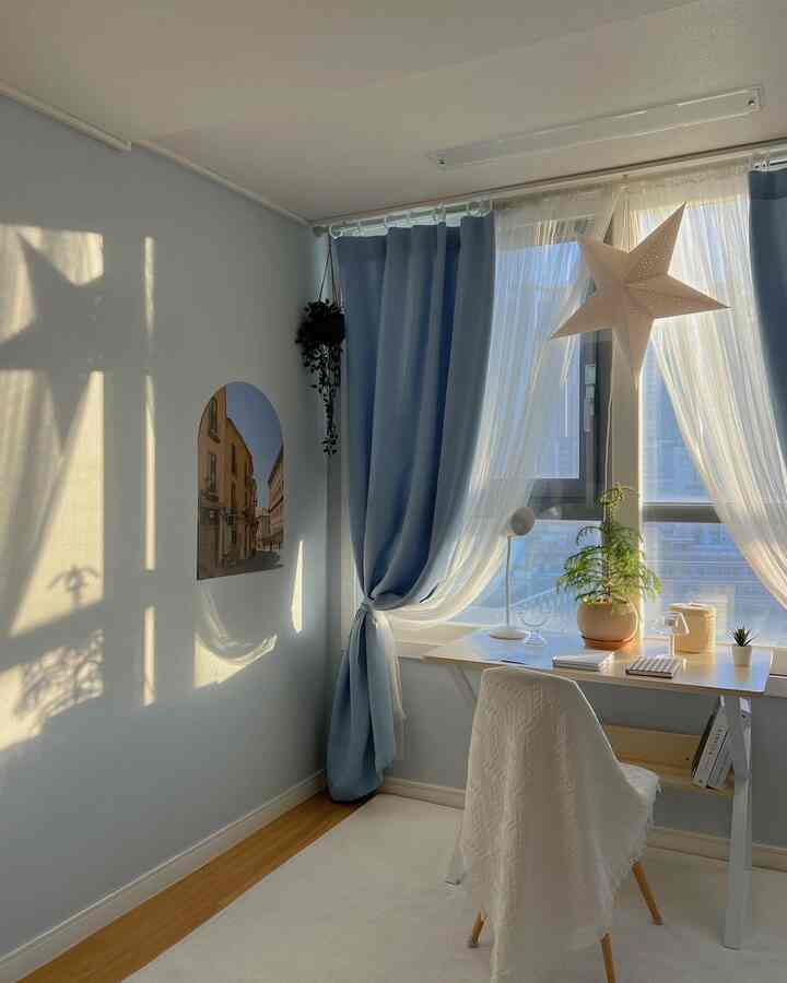 スカイブルーの壁紙とカーテンが調和した子供部屋、窓辺に配置されたデスクと植物が明るく温かみのある雰囲気を作るインテリア