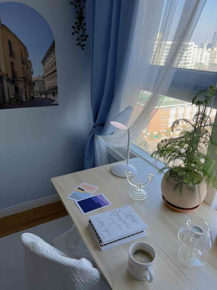 Pastel-toned home office space with blue curtains, transparent candle holder, plant, and desk arranged neatly