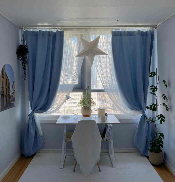 Soft white and sky blue kids' room featuring a desk and plants by the window with a tidy reading setup