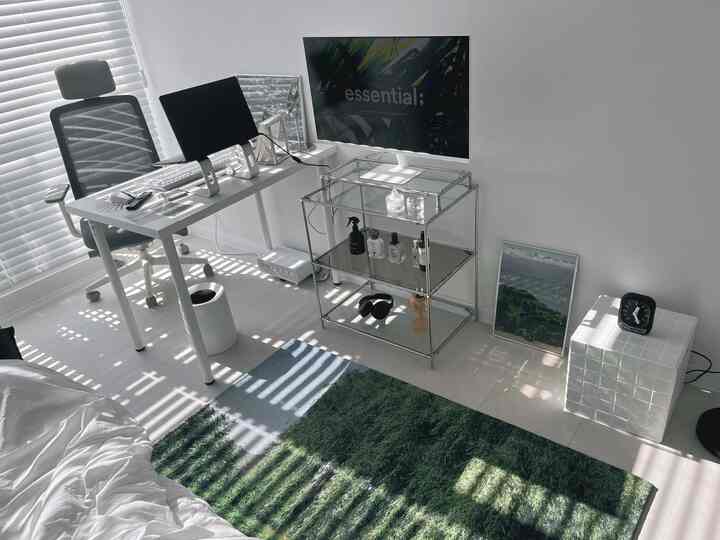 White and green toned home office space featuring a clean desk, ergonomic office chair, and green rug with a simple modern interior