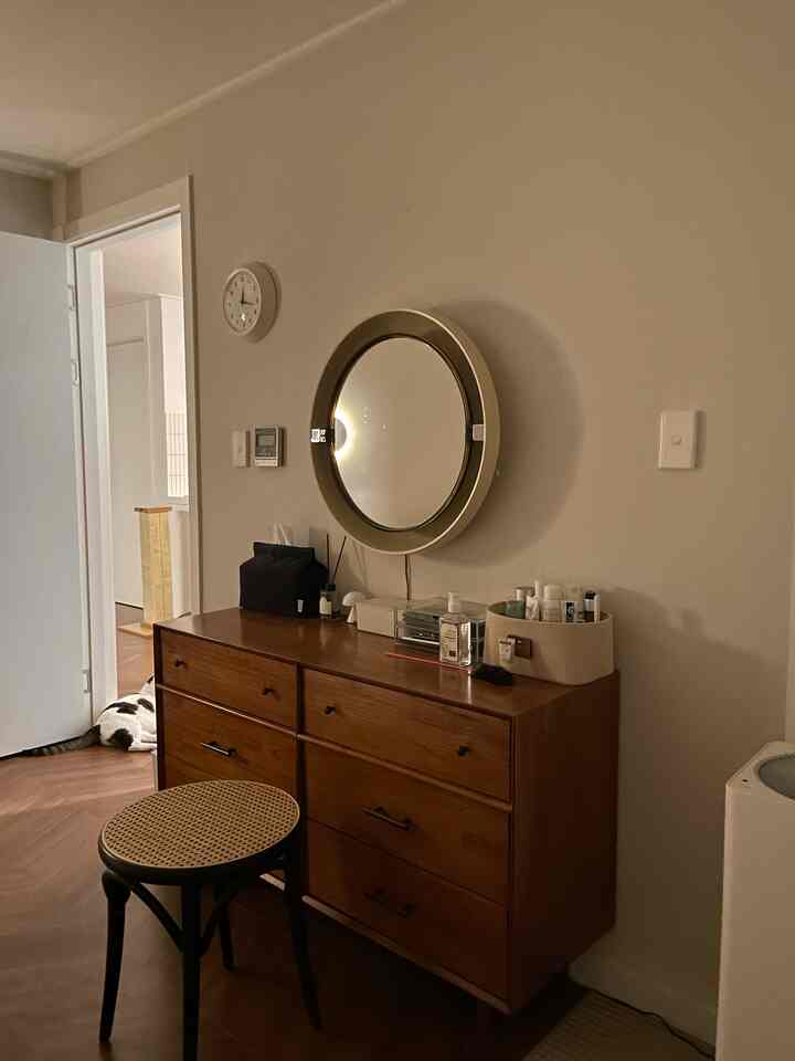 白い壁とブラウンの木製チェストがある玄関スペース、丸い鏡と椅子が配され、自然で落ち着いた雰囲気のインテリア