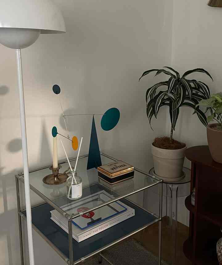 Natural and clean living room corner featuring white walls, silver metal framed glass side table with objets and potted plants