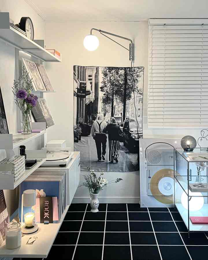 Modern living room in white and black tones featuring a large poster, blinds, and a grid-patterned rug creating a calm atmosphere