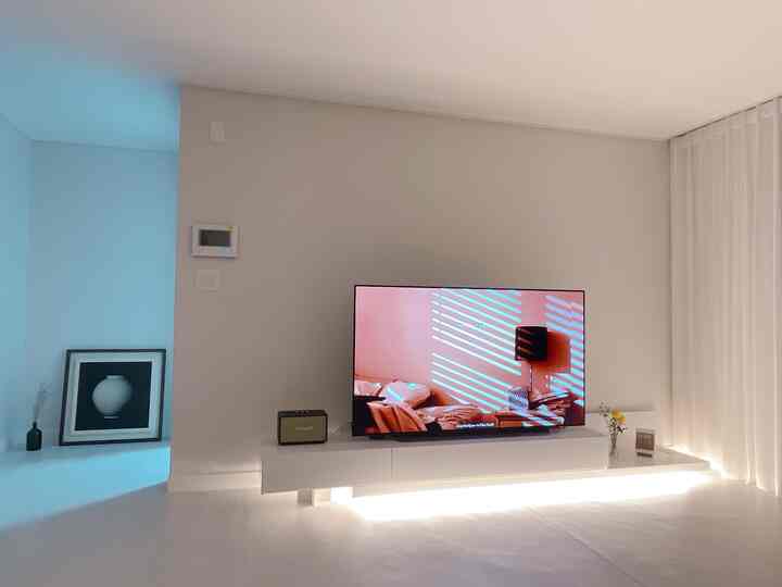 White-toned living room featuring wall-mounted TV and minimalist TV stand, creating a modern and simple interior atmosphere
