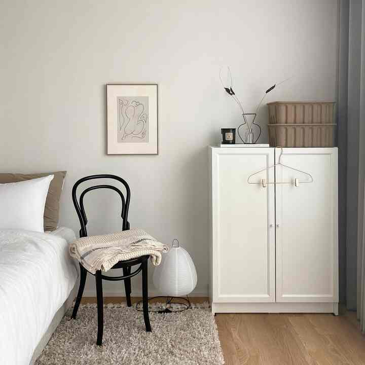 White and beige toned bedroom featuring a white bed, black chair, and white storage cabinet in a simple setting