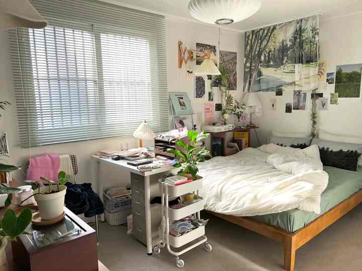 Bright white and natural wood-toned studio bedroom featuring desk, bed, and plants creating a cozy atmosphere