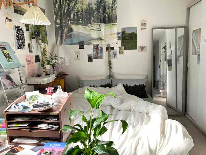 A cozy 6-tatami bedroom with white walls and bedding, natural wooden storage, featuring green plants and poster decorations
