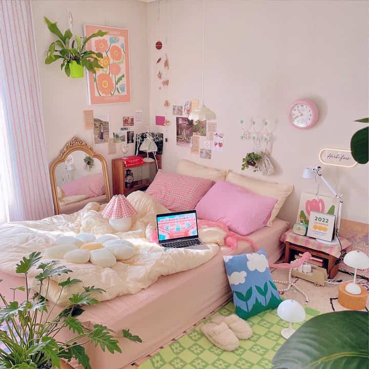 ピンクと淡い黄色の色調の寝室、花柄のポスターと植物が配置された温かみのある雰囲気のインテリア