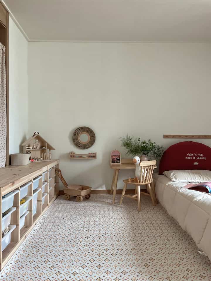 ベージュと白の色調の子供部屋、木製家具と赤いベッドヘッドが配置された自然なモダンなインテリア