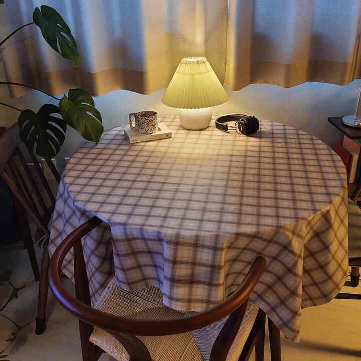 ベージュとブラウンのトーンのダイニングテーブル、チェック柄のテーブルクロス、テーブルランプが配置された落ち着いた小さなリビング空間