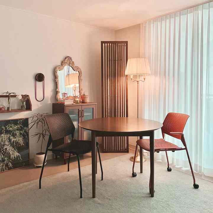 Warm light brown and white-toned living room featuring a round table, two chairs, sheer curtains, and a floor lamp in a simple vintage style