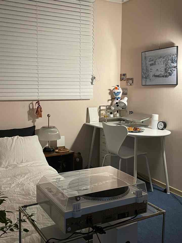 White and beige-toned bedroom and home office space featuring a bed, desk with laptop, and LP turntable in a cozy atmosphere