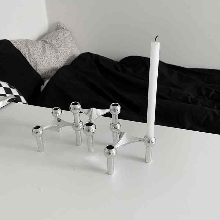 A simple space showcasing a modern silver candle holder with a white candle on a white and silver-toned table