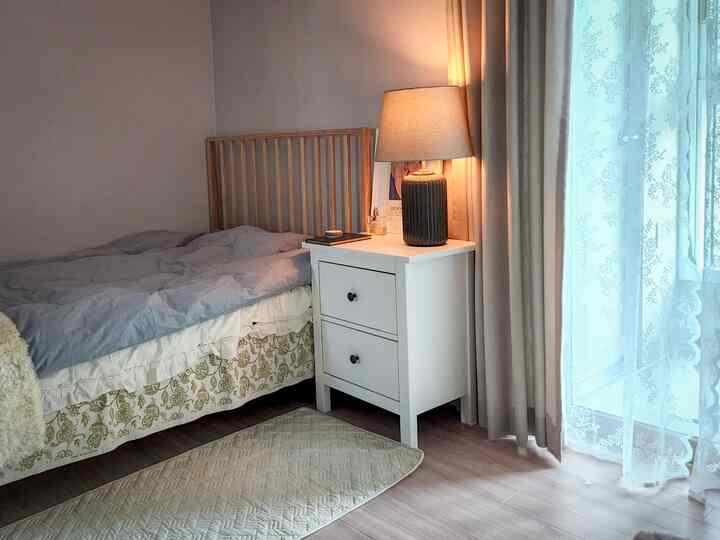 Natural tone bedroom featuring a wooden bed frame, white nightstand, and warm table lamp creating a cozy atmosphere