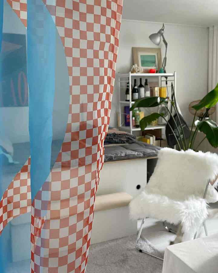 White and gray toned studio bedroom featuring checkered curtain, floor lamp, and storage shelf in a cozy interior