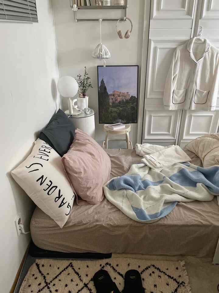 ベージュとナチュラルトーンの寝室、枕とスローが置かれた快適な一人用ベッドとサイドテーブルのある空間