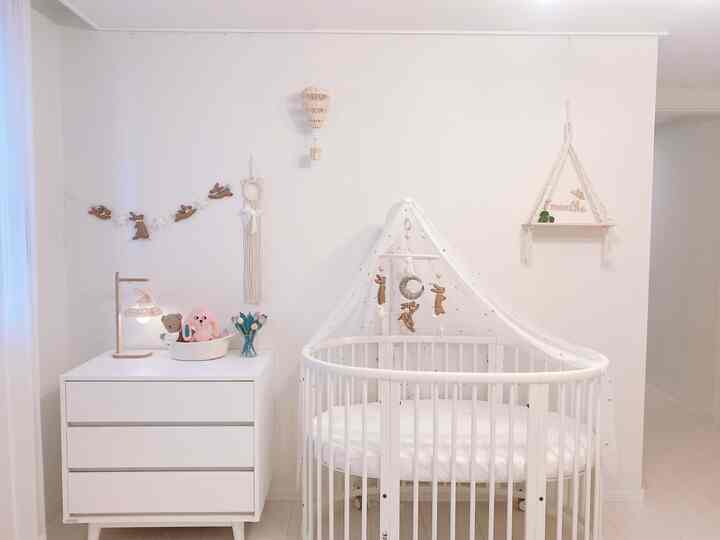 White and natural toned baby room featuring round crib and rattan pendant light with calm atmosphere