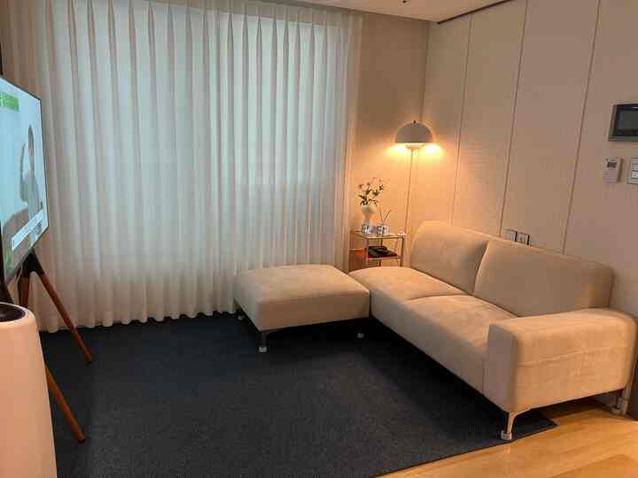 ホワイトとネイビートーンのコンパクトなリビング、ホワイトのソファとスツールが配置され、大きな白いレースカーテンが窓を覆っている雰囲気のあるインテリア