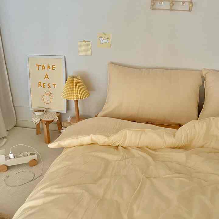Soft light brown tone bedroom featuring beige bedding, a small wooden stool, and a table lamp creating a cozy atmosphere