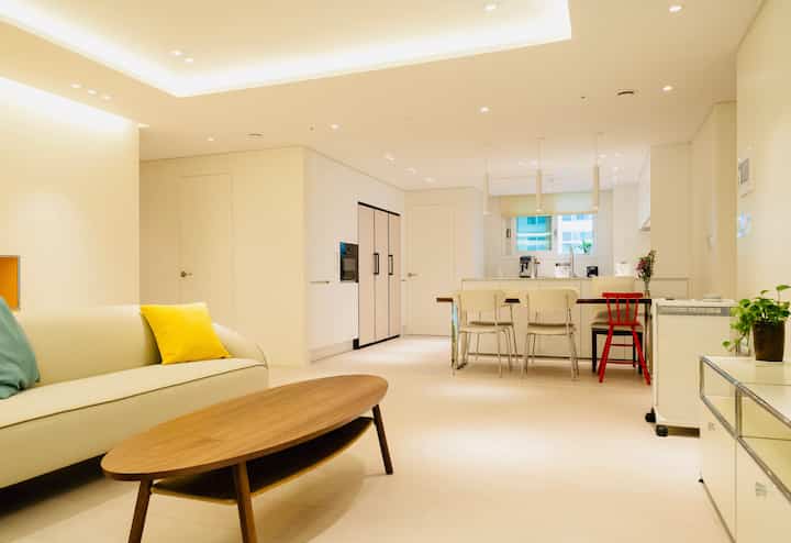 A natural modern living room in cream beige and wood tones featuring a neat open kitchen layout