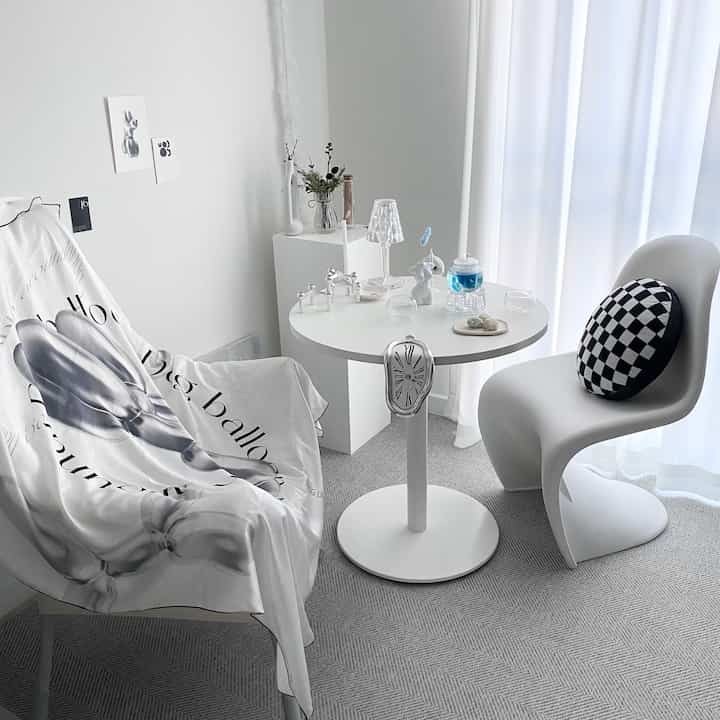 A modern and simple round room in white and gray tones featuring a round table, chairs, and delicate interior accessories