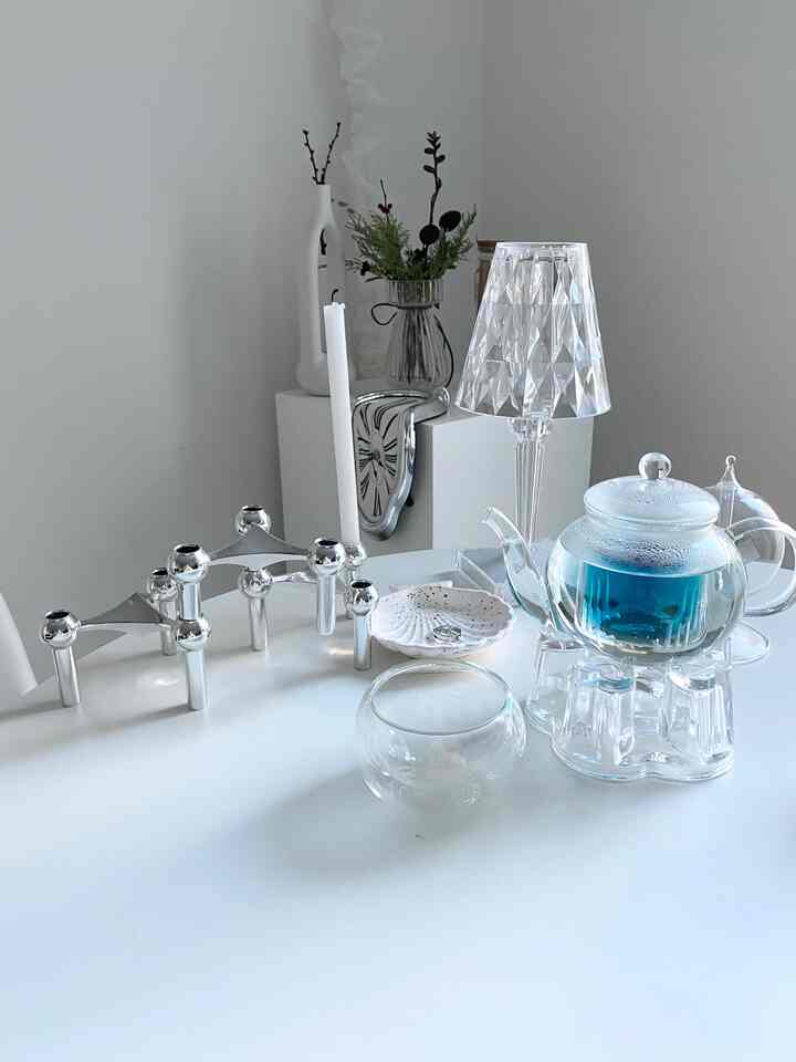 Modern white interior accessories featuring transparent glass teapot and teacup arranged on a clean, sleek surface