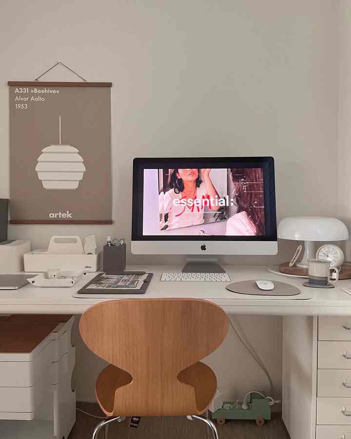 Minimal home office with white walls and natural wood chair, featuring an iMac and table lamp in a clean study space