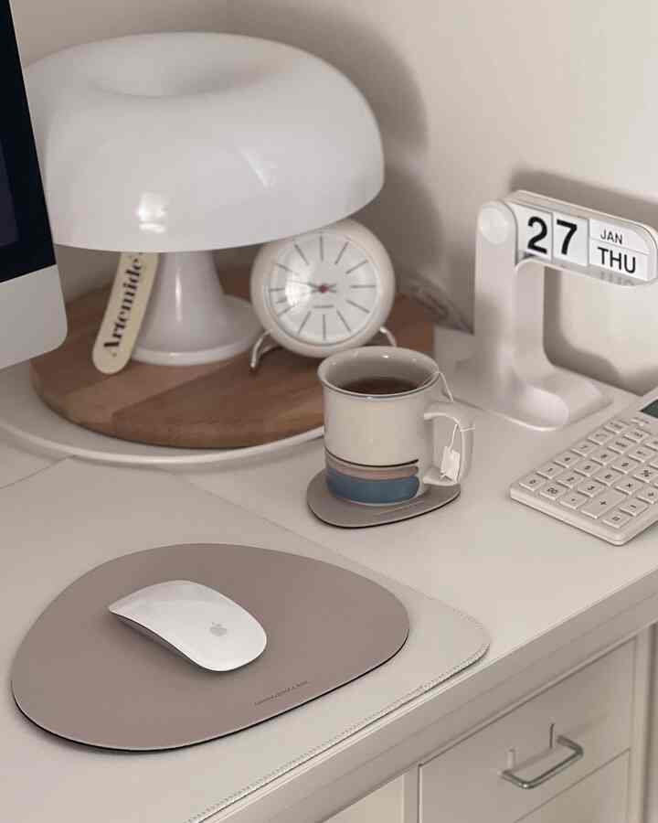 White-toned home office featuring Artemide Nessino lamp, desk clock, and leather mouse pad on a neat workspace