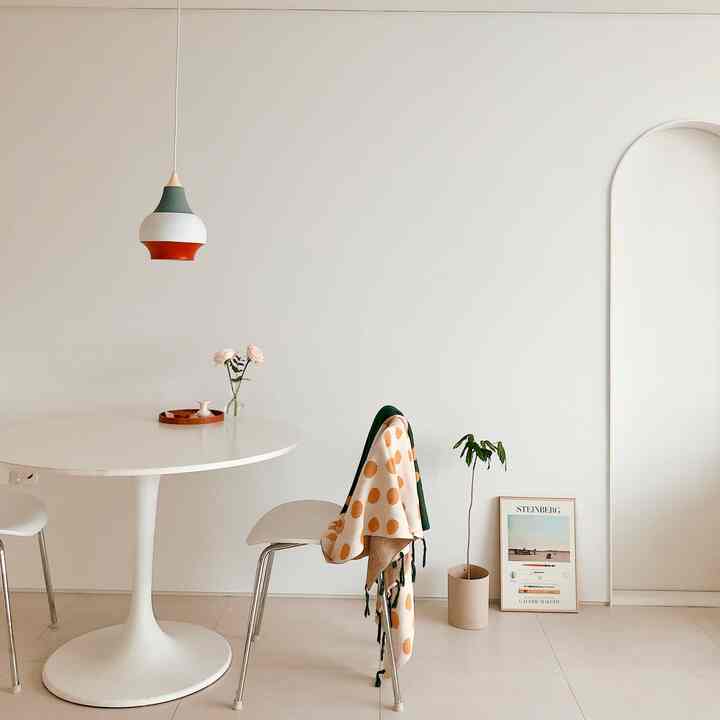Simple dining room in white and beige tones featuring a round dining table, chairs, and a pendant light