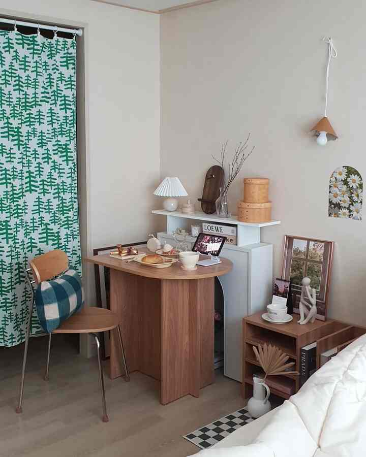 A beige and wood tone bedroom space featuring a dining table with chair, curtain, and picture frames with a cozy natural home cafe vibe