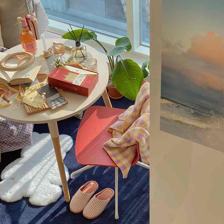 明るい日差しの中、ネイビーのラグと丸いダイニングテーブル、チェック柄のスローとスリッパが調和した温かみのあるリビングルーム