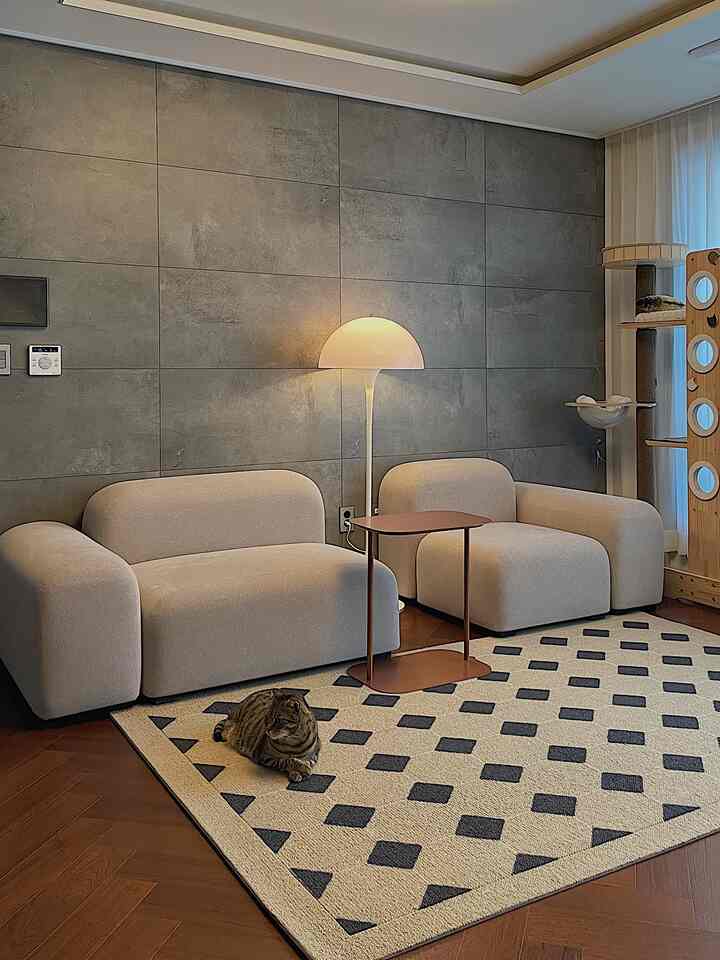 Cozy living room featuring warm wood flooring and stylish gray wall, beige modular sofas with patterned rug, accompanied by a cat and cat tower