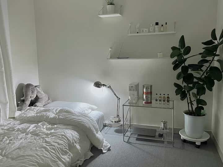 A white-tone and gray-floor studio bedroom featuring minimal modern furniture and a coffee machine creating a cozy space
