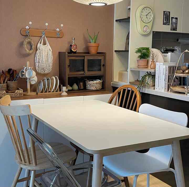 Kitchen with brown walls and natural wood tone furniture, featuring diverse dining chairs and abundant vintage-style decor items