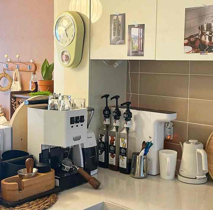 明るいベージュとホワイトの色調のキッチン、コーヒーマシン、電気ケトル、シロップボトルがかわいらしく配置されたおうちカフェのインテリア